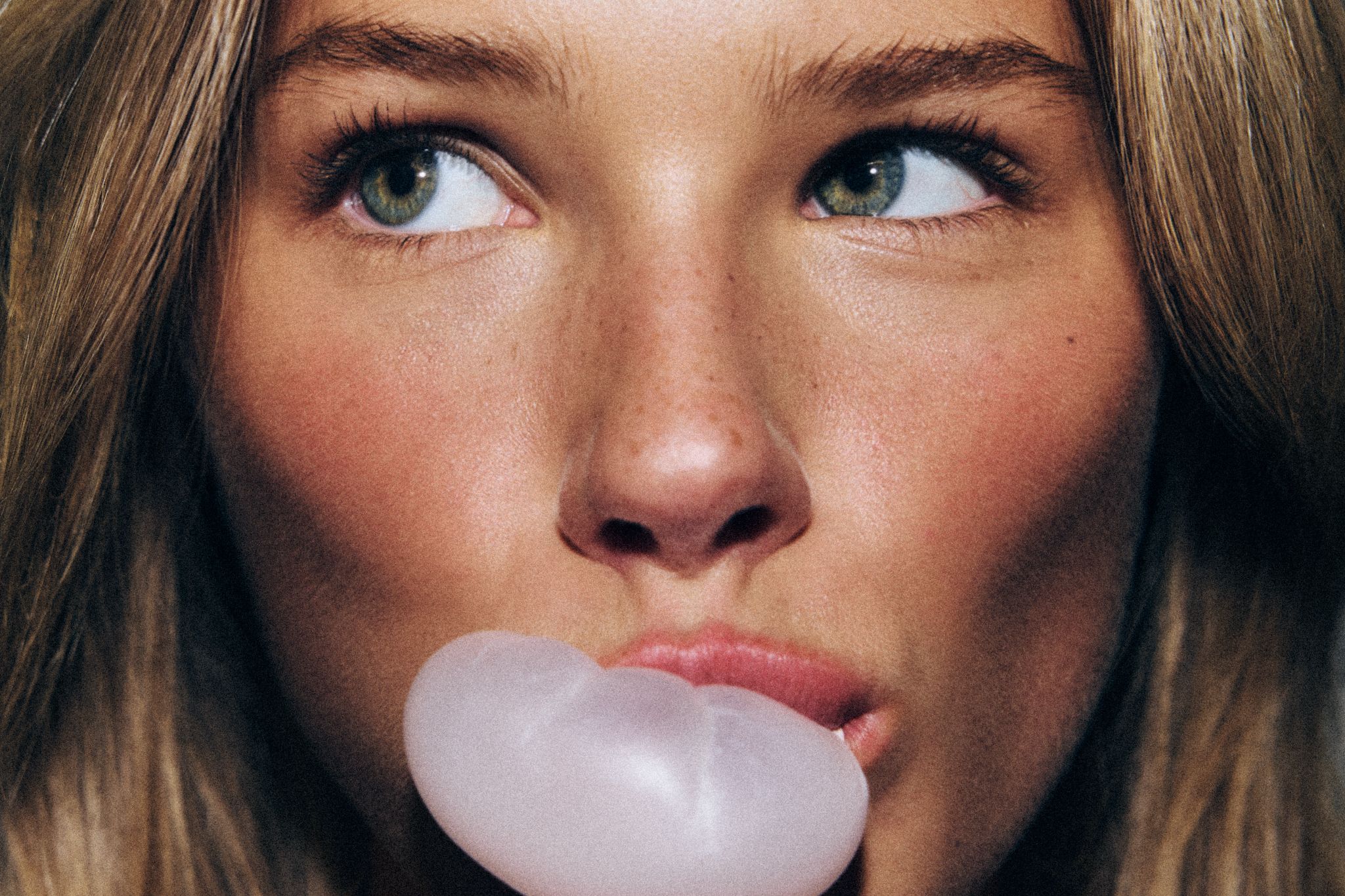 visage d'une femme en train de faire une bulle avec son chewing-gum